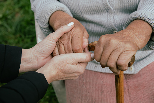 Caregiver holding hands of an unrecognizable senior woman with a cane