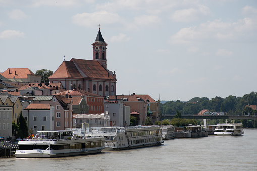 Passau, Germany - July 22, 2021: Danube river cruise boats docked near the Stadtpfarrkirche St. Paul (Town Parish Church of St. Paul).
