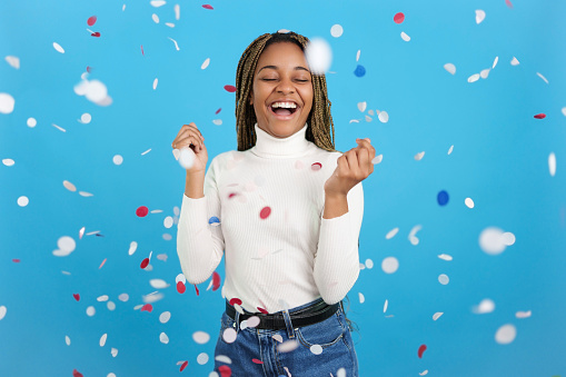 Studio portrait with blue background of an excited African woman surrounded by flying confetti