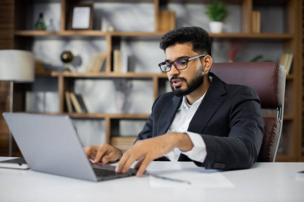 istock Confident young middle eastern businessman sitting at work table at modern office, speaking with customers 1449990558