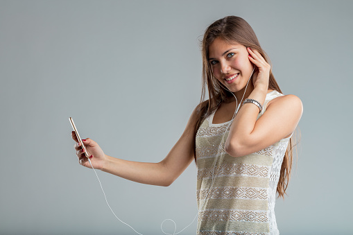 I'm listening and watching, can I help you? concept of beautiful young woman with smartphone and earphones plugged in interrupting to give you attention