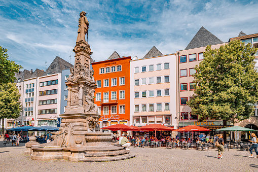 29 July 2022, Cologne, Germany: People walking and resting in cafe at old market square with historic statue in Koln. City life and urban development
