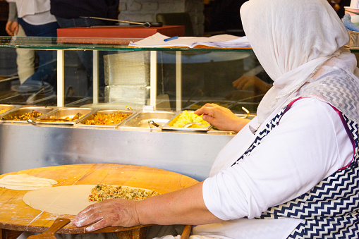 Nov 5 , 2022 - Istanbul, Turkey: Anonymous Turkish woman with hijab preparing traditional gozleme on wooden table. Restaurant chef cooking stuffed dough bread in Istanbul, Turkey