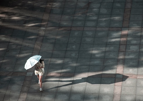 A high angle shot of a female with an umbrella walking on the street on a sunny day