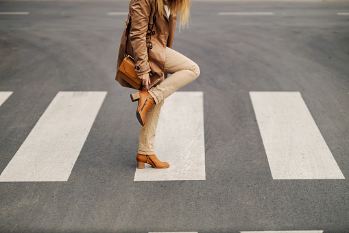 Cropped image of a fashionable woman standing in the middle of the road and adjusting her heels.