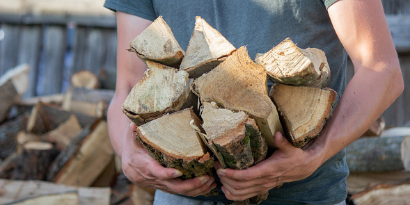 A man holds a lot of chopped firewood in his hands. Selective focus