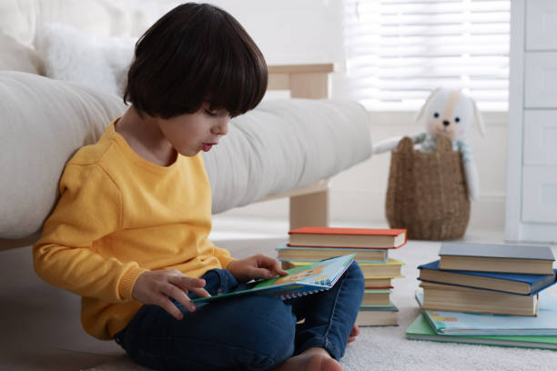 istock Cute little boy reading book on floor at home 1450003373
