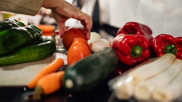istock A female chef holding and picking a fresh tomato from vegetables on the table 1450004734