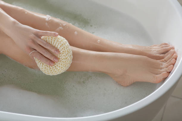 istock Woman rubbing her leg with sponge while taking bath, closeup 1450004936