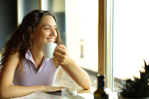 Happy woman holding coffee in a restaurant looks away