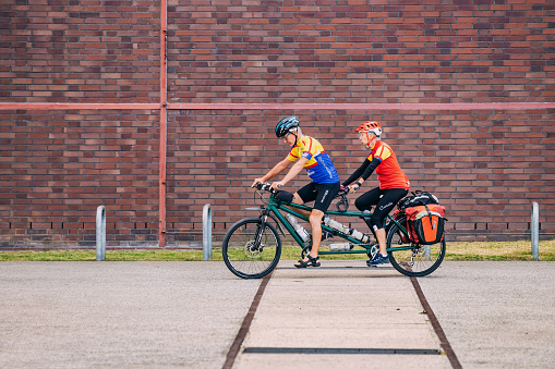 27 July 2022, Zollverein, Essen, Germany: An elderly senior fit and sporty couple travelling and riding a tandem bicycle and explore the sights of the old town