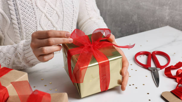 istock Woman wrapping Christmas gift at white marble table, closeup 1450006745