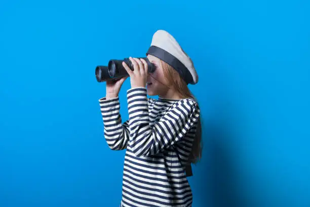 A teenage girl in a sailor suit with a binocular looking into the distance, Horizontal portrait of a sailor girl on a blue background
