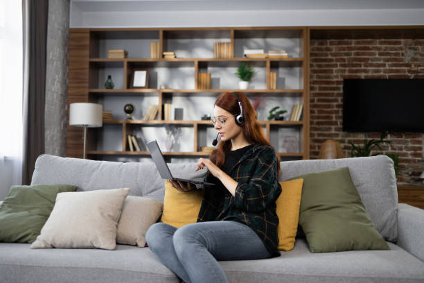 istock Young red hair business woman working on computer, talking online using a headset 1450008556