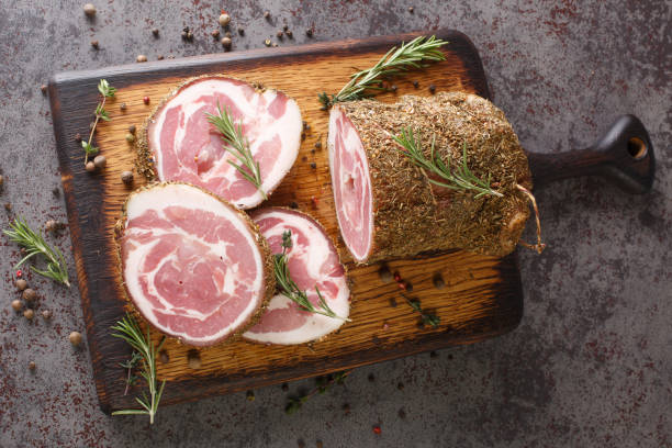 pancetta est une poitrine de porc séchée faite de sel, d’herbes et d’épices en gros plan sur la planche de bois. vue de dessus horizontale - round of beef photos et images de collection