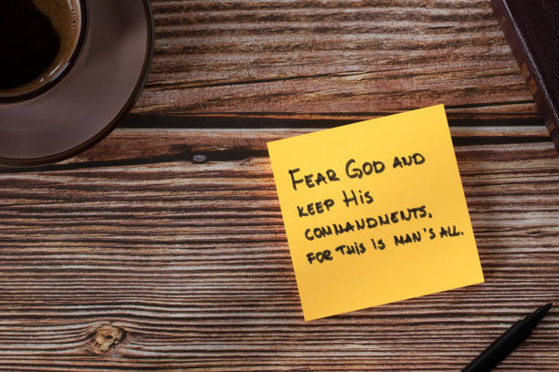 istock Fear God and keep His commandments, handwritten verse on yellow note with bible book and coffee cup on wooden table, top view 1450012391