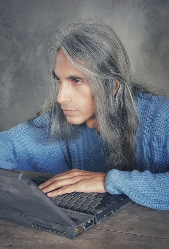 Long haired man in pensive mood in front of vintage laptop