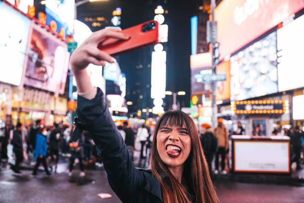행복한 여자는 타임 스퀘어에서 셀카를 찍어 소셜 미디어에 공유합니다. 스톡 사진