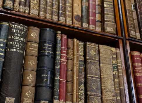 Collection of books arranged in a row of various religions bound in brown leather on a wooden shelf