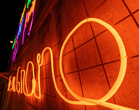 Illuminated letters and words made with neon lights and LEDs of many colors with a vanishing point in the background. Wires and tubes linked to create shapes.
