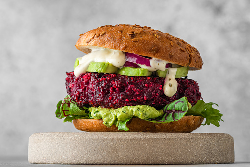 Vegan burger with beetroot cutlet, avocado and vegan mayo sauce on gray background. Healthy veggie food