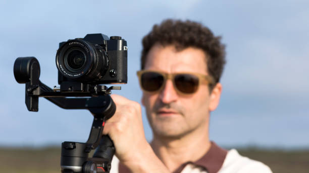 istock Camera operator recording video with a handheld Gimbal stabilizer. Outdoor content creator with a handheld gimbal stabilizer. Selective focus and blurred background. videography with 3-axis stabilizer 1450024814