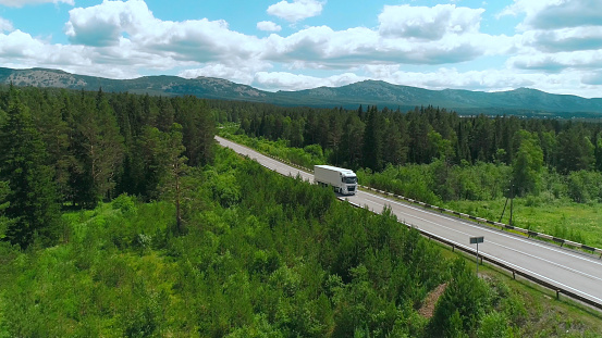 Top view of truck driving along highway on summer day. Scene. White truck is driving on country highway with green wooded area. Truckers and moving trucks in summer.
