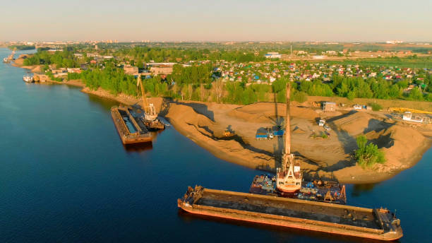 vue à vol d’oiseau. la rivière sur laquelle il y a des navires pour la construction avec des cargaisons sur eux et une ville lumineuse avec des arbres d’été verts contre un ciel bleu est visible. - construction built structure building activity shipyard photos et images de collection