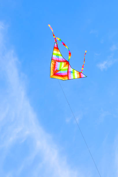 istock rainbow colored kite flying high in the blue sky with some white clouds 1450028933
