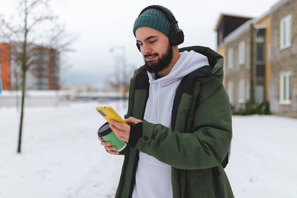 istock Handsome young man with a beard using his phone outdoors while wearing headphones 1450037219