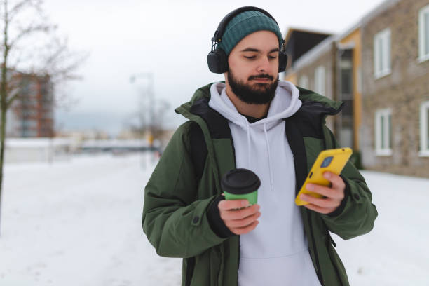 istock Handsome young man with a beard using his phone outdoors while wearing headphones 1450037224