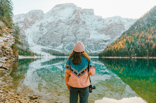Young Caucasian woman with camera standing on the background of  Lago di Braies in winter