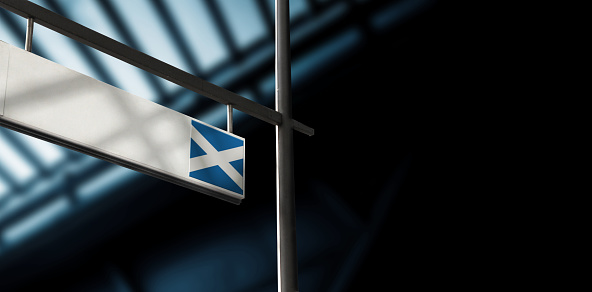 Flag of Scotland on airport departure information board. Close-up. Roof construction in the background. Blue color. Horizontal orientation. Ne people. Copy space.