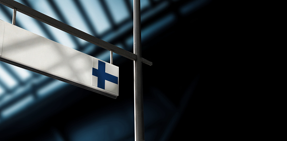 Flag of Finland on airport departure information board. Close-up. Roof construction in the background. Blue color. Horizontal orientation. Ne people. Copy space.