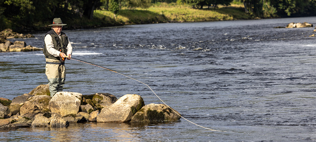 Pitlochry, Scotland - September 13, 2022: Scottish Fly fisherman stands quietly as he leaves his fly to lie for Salmon in the turbulent waters of the River Tummel