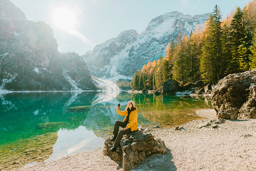 Young caucasian woman   photographing on smartphone near Lago di Braies in winter