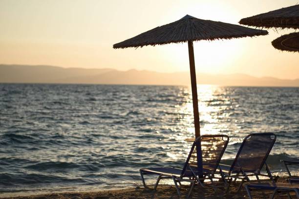 istock Selective focus of beach chairs under umbrellas with a sunset view over the blue sea in the backdrop 1450048310