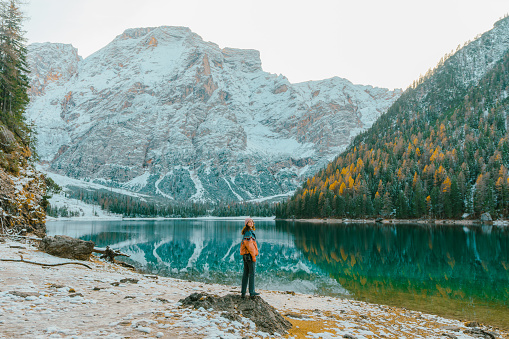 Young Caucasian woman with camera standing on the background of  Lago di Braies in winter