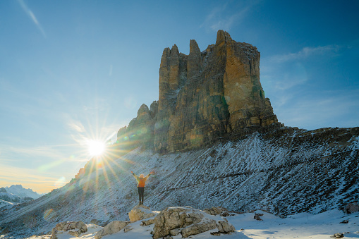Young Caucasian woman with raised arms on the background of Tre Cime di Lavaredo in winter