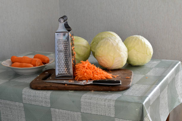 Heads of cabbage, carrots and tools for chopping and pickling cabbages lie on the kitchen table on a cutting board and nearby.