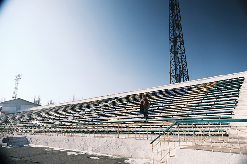 Woman is looking down from the stands of old inactive stadium in Karakol, Kyrgyztan (This stadium is the open area where everyone can enter without any permission or ticket or fee. No competitions or another events take place on this stadium for a long time)
