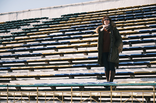 Woman is looking down from the stands of old inactive stadium in Karakol, Kyrgyztan (This stadium is the open area where everyone can enter without any permission or ticket or fee. No competitions or another events take place on this stadium for a long time)
