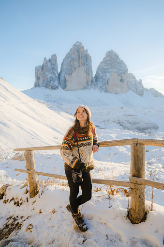 Young Caucasian woman with camera hiking  on the background of Tre Cime di Lavaredo in winter