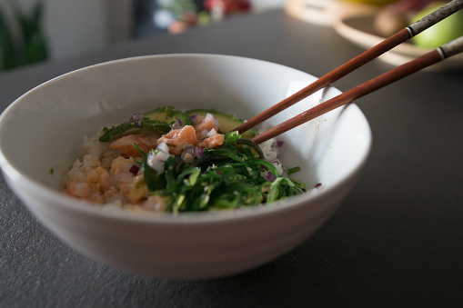 Close up of a bowl with salmon poke and chopsticks. Home interior