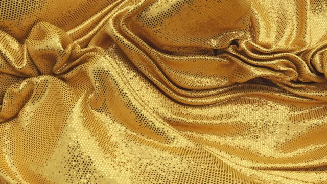 Gold sequin fabric curling into a wrinkled surface.