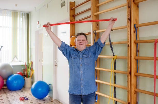 a young man with down syndrome is engaged in a gym with a gymnastic stick. rehabilitation process. a young man with down syndrome is engaged in a gym with a gymnastic stick. rehabilitation process сербия stock pictures, royalty-free photos & images