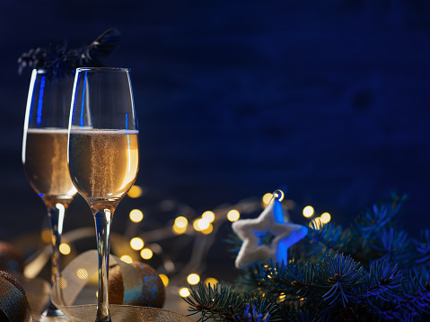 Two glasses of champagne or sparkling wine on a festive Christmas table with copy space. Blue background