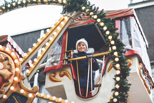 Happy cute preschool girl riding on ferris wheel carousel horse at Christmas funfair or market, outdoors. Little toddler child having fun on traditional family xmas market in Germany
