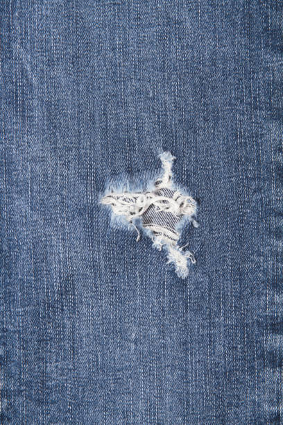 istock vertical image - Hole and Threads on Denim Jeans. Ripped Destroyed Torn Blue jeans background. Close up blue jean texture 1450082254