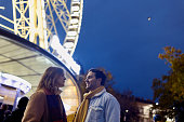 Young couple standing in front of a ferris wheel in a public park